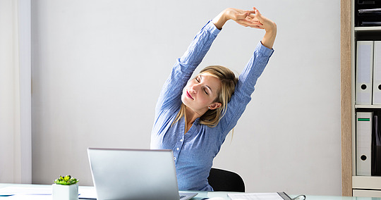 Frau streckt Arme während der Arbeit am Laptop