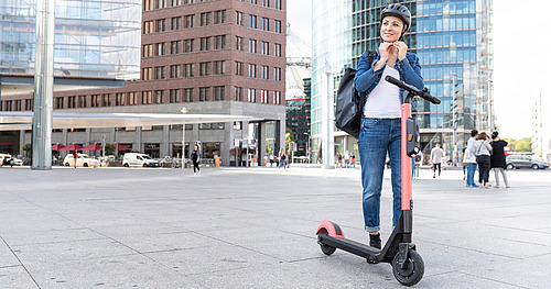 Frau mit E-Scooter setzt sich gerade einen Helm auf
